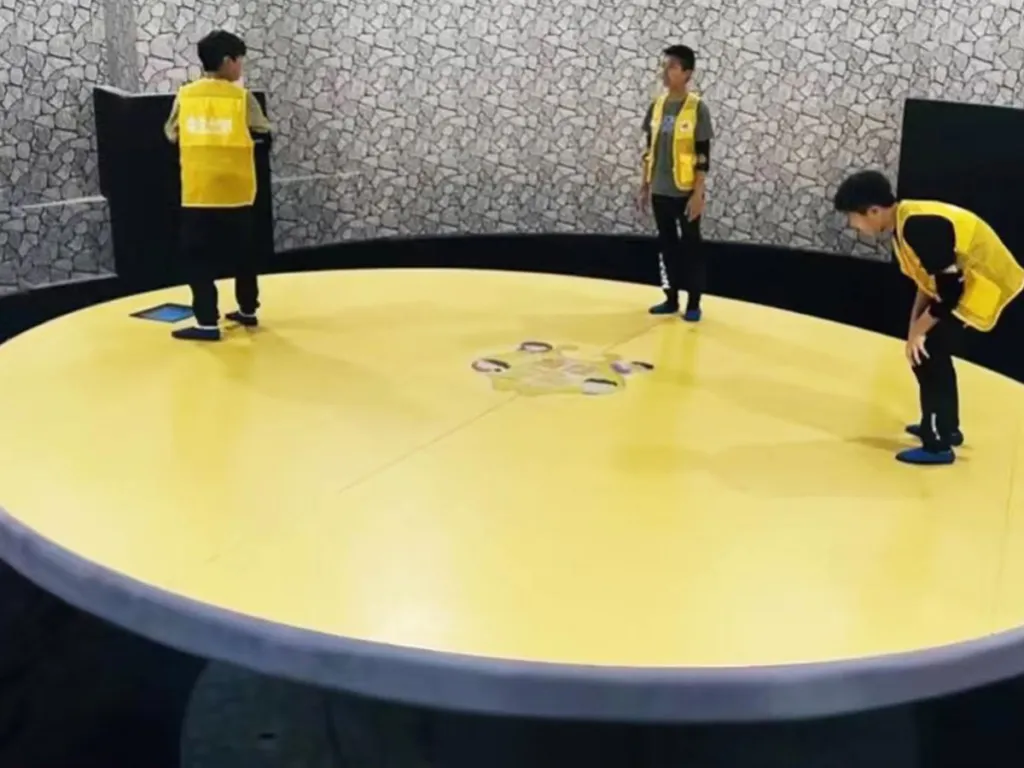 Balance-Scheibe von Cheer Amusement: große runde Plattform, auf der drei Spieler das Gleichgewicht halten